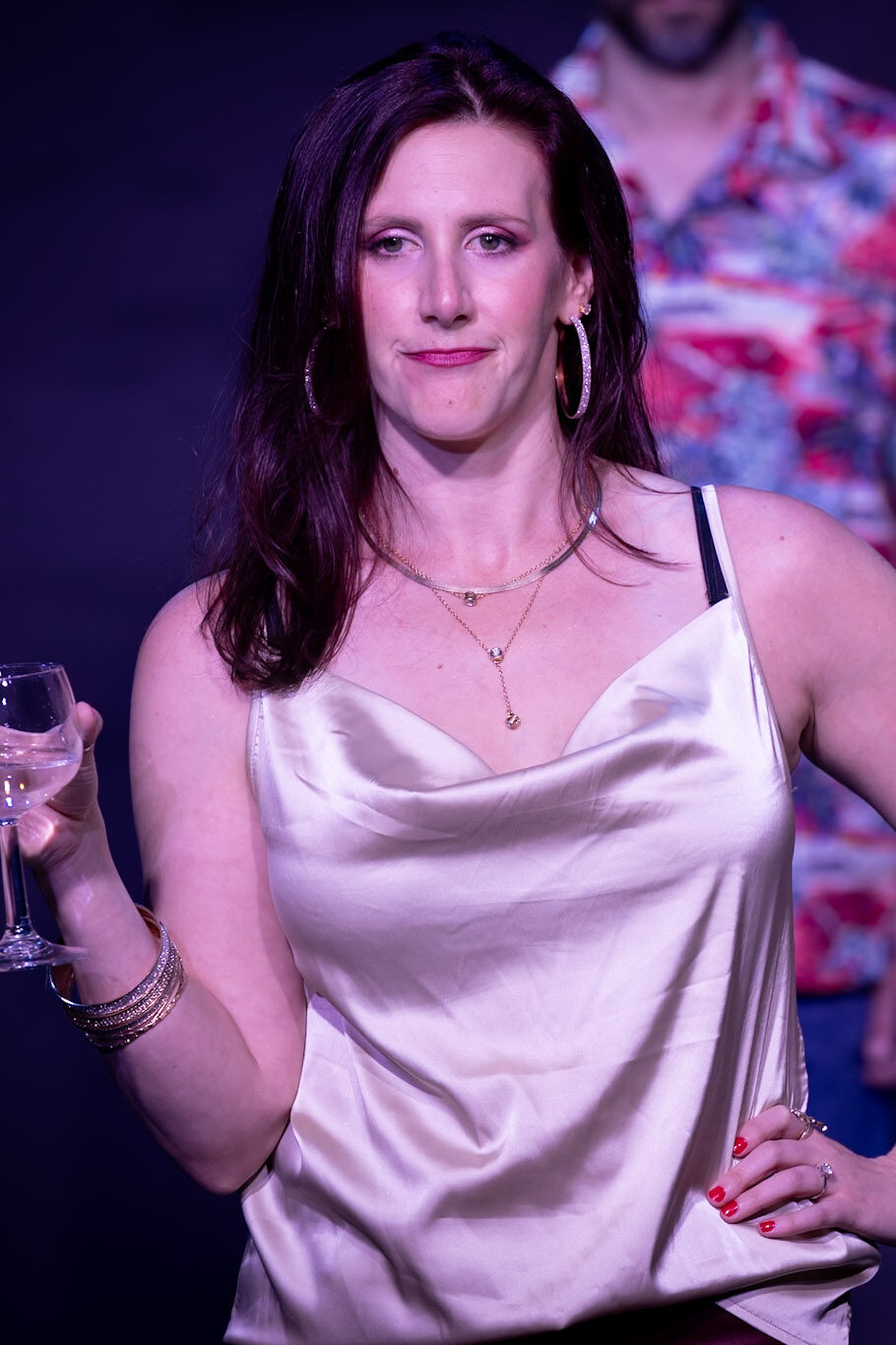 Woman holding wine glass on stage with necklace.